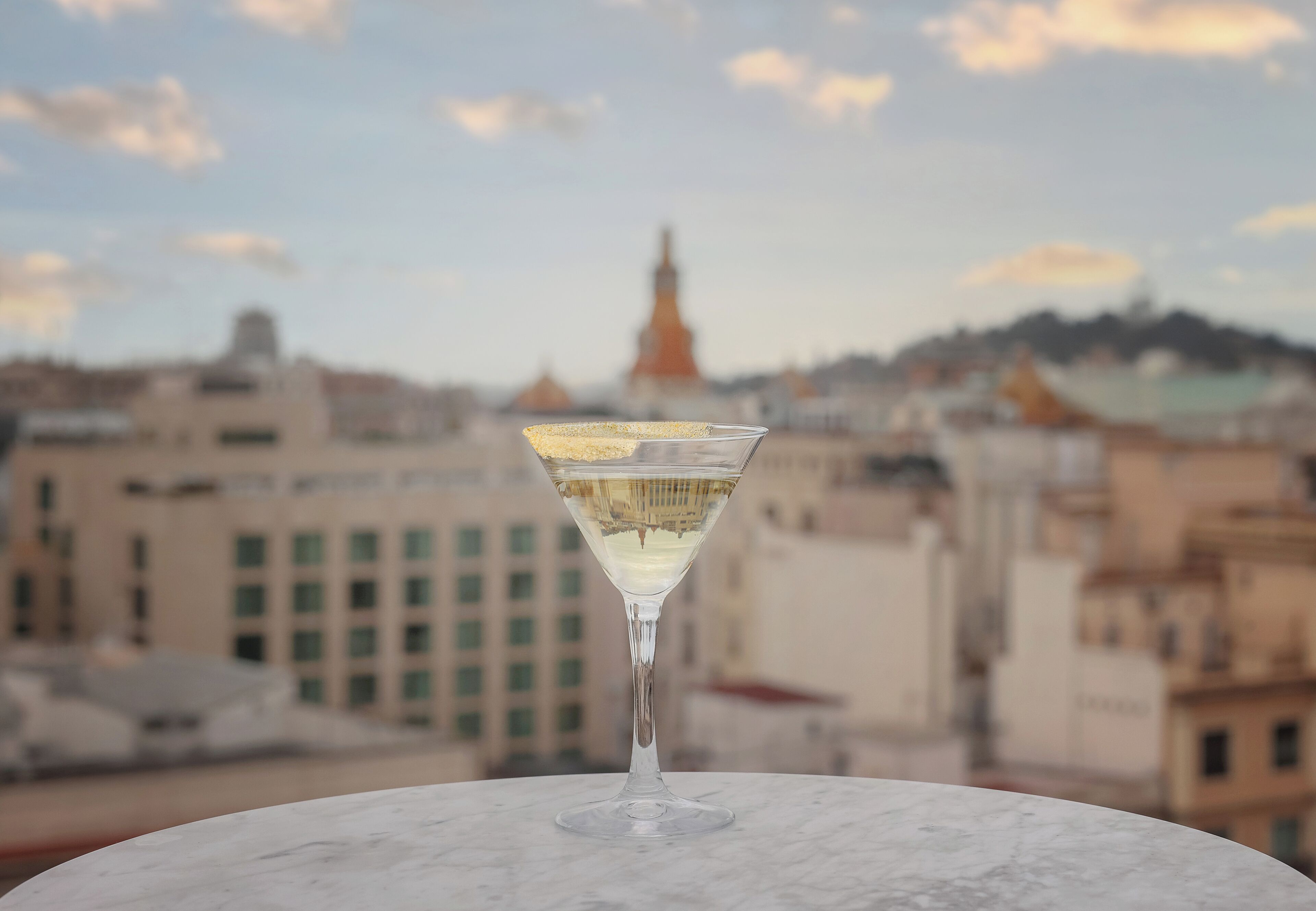 A martini glass on a marble table with a cityscape in the background.