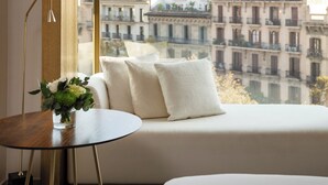 A modern hotel room with a large window, a round wooden table, and a sofa with cushions.