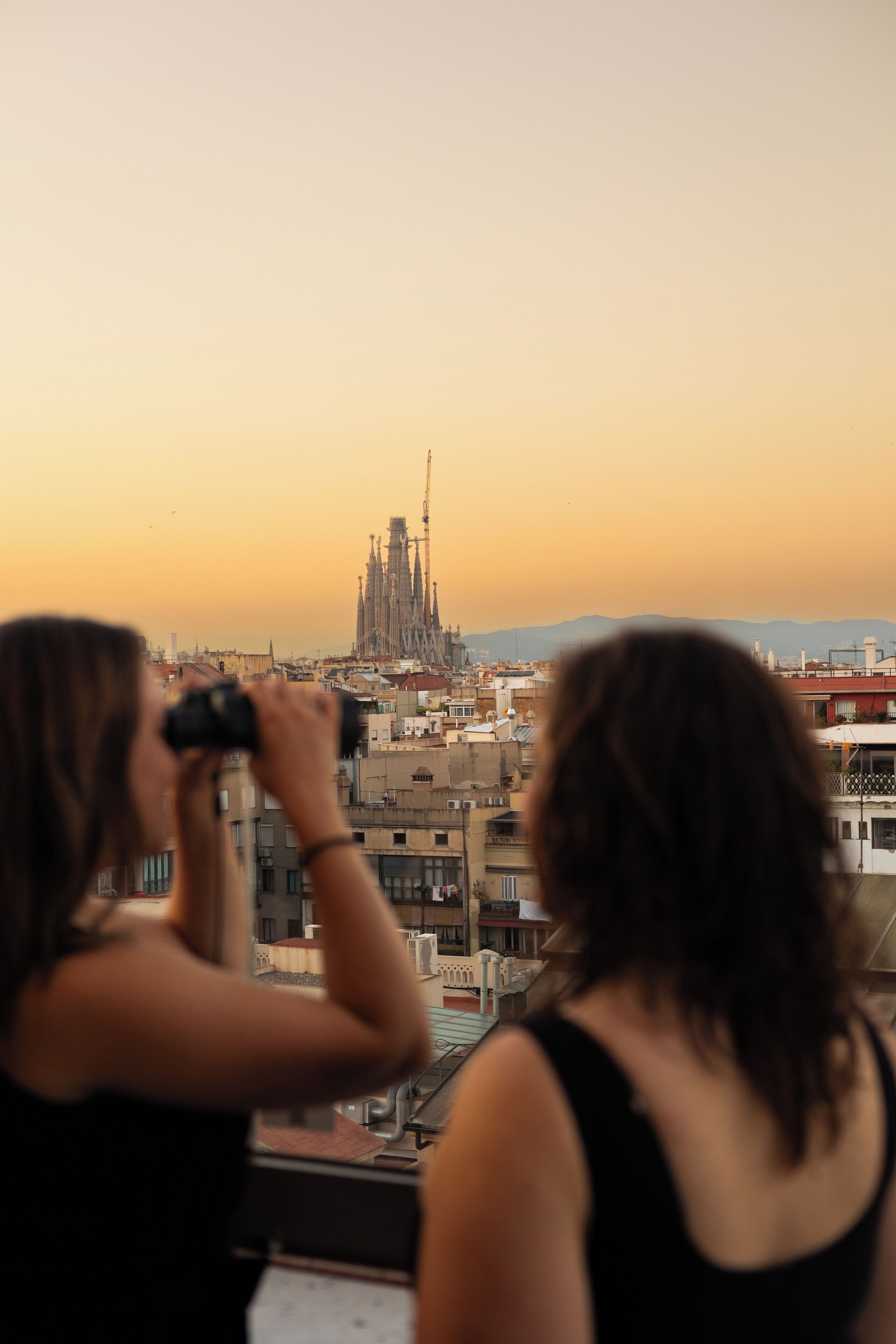 Deux personnes prennent une photo d’un bâtiment doté d’une flèche, vraisemblablement une cathédrale, depuis un balcon ou une terrasse.
