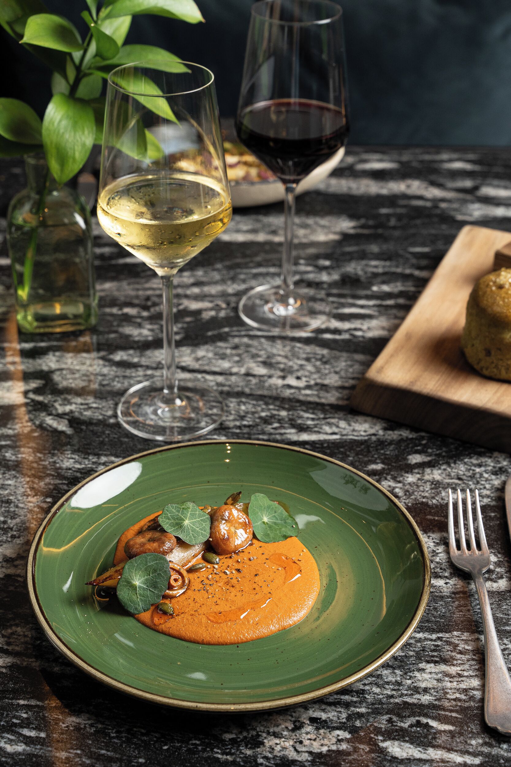 Une table à manger avec une assiette verte remplie de nourriture, deux verres à vin et une fourchette.