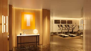 A modern hotel lobby with a wooden reception desk, a large illuminated 'T' sign, and a row of exercise bikes.