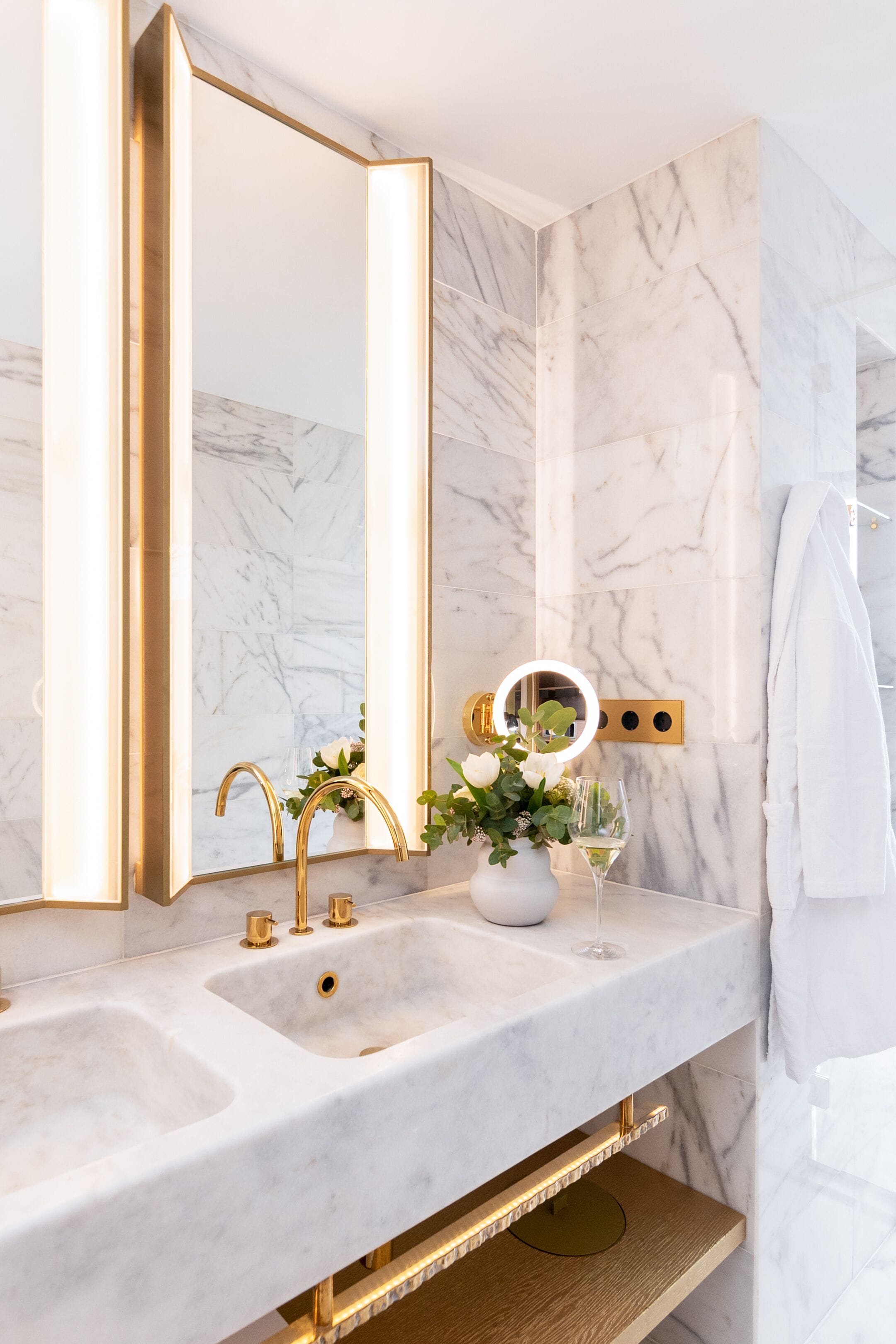 A bathroom with a marble vanity, gold fixtures, and a mirror with integrated lighting.
