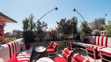 Un área de estar al aire libre con sofás y sillones a rayas rojas y blancas, una mesa redonda y dos farolas.
