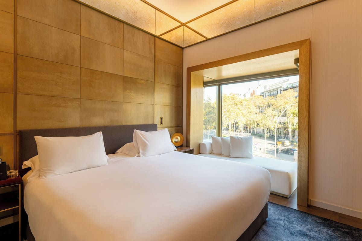 A large bed with white linens, a wooden headboard, and a nightstand with a lamp.