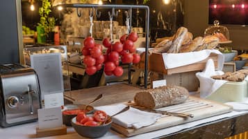 Un bufé de desayuno con varias opciones de pan y pan de tomate, un cortador de pan y un bol de tomates.