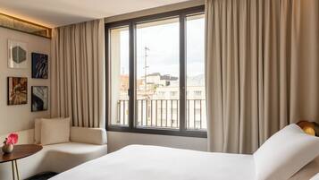 Una habitación de hotel con una cama grande, un sofá, una mesita con un jarrón y una ventana con cortinas.