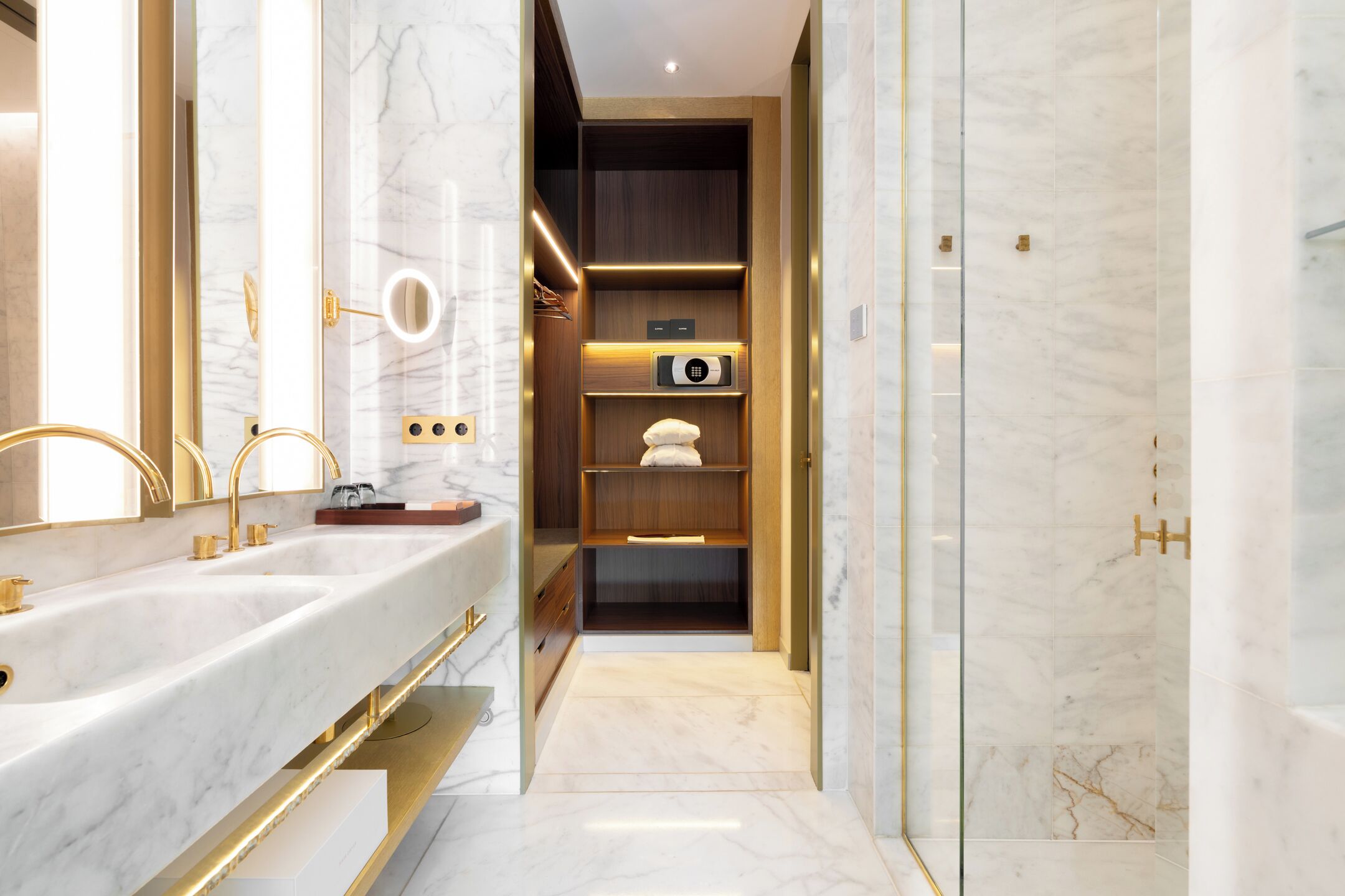 Une salle de bain moderne dotée d’un meuble-lavabo à deux vasques, d’une douche à l’italienne et d’étagères intégrées, ainsi que d’un miroir et d’un porte-serviettes.