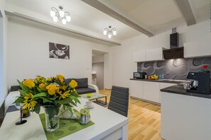 A modern kitchen with white cabinetry, a dining area with a table and chairs, and a living area with a sofa.