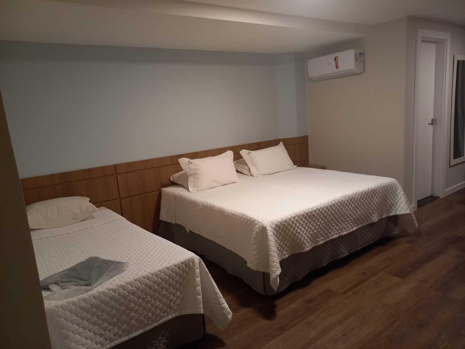 Camera d'albergo con due letti, testiere in legno e un muro bianco con condizionatore.