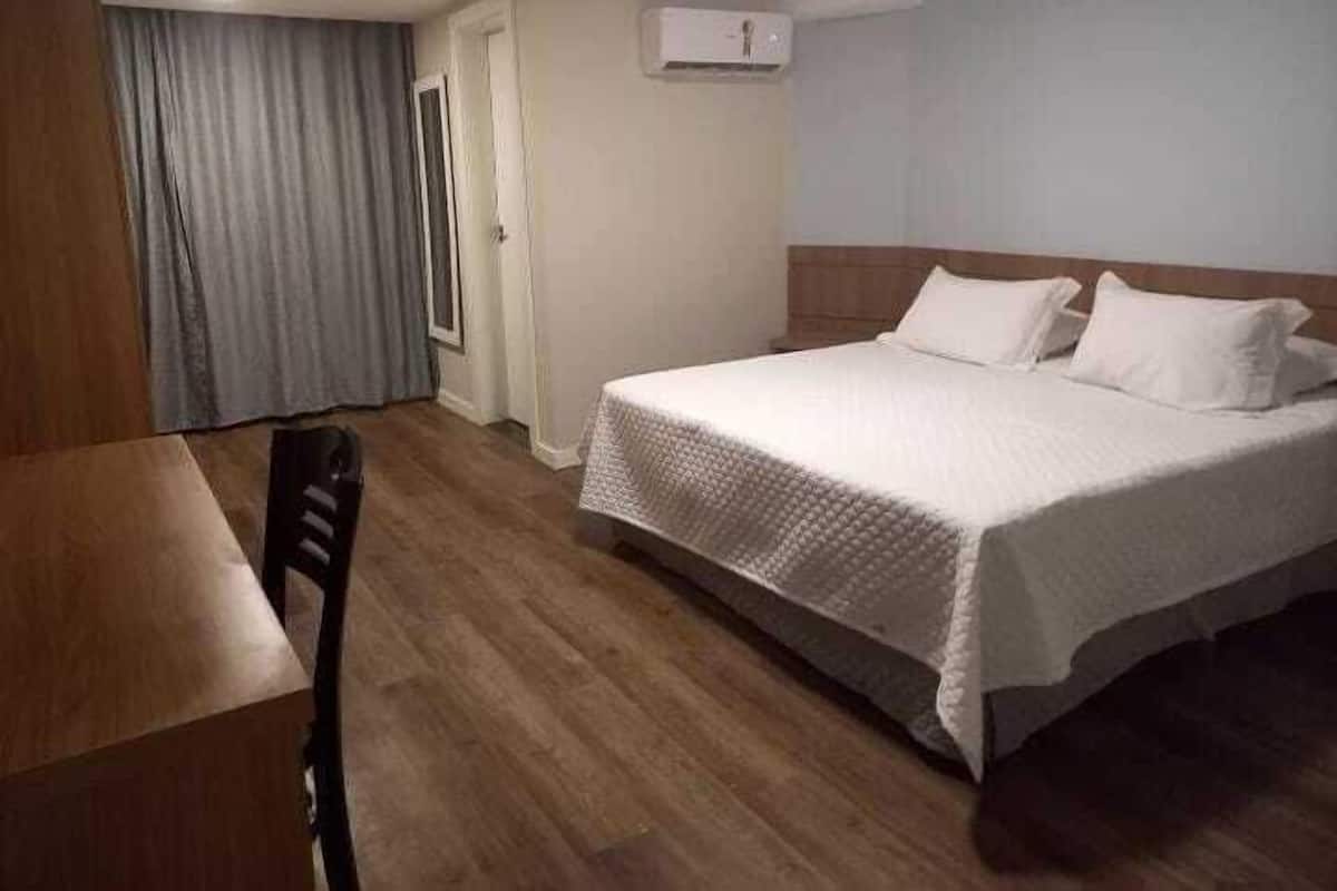 A hotel room with a bed, a chair, a table, and a window with curtains.