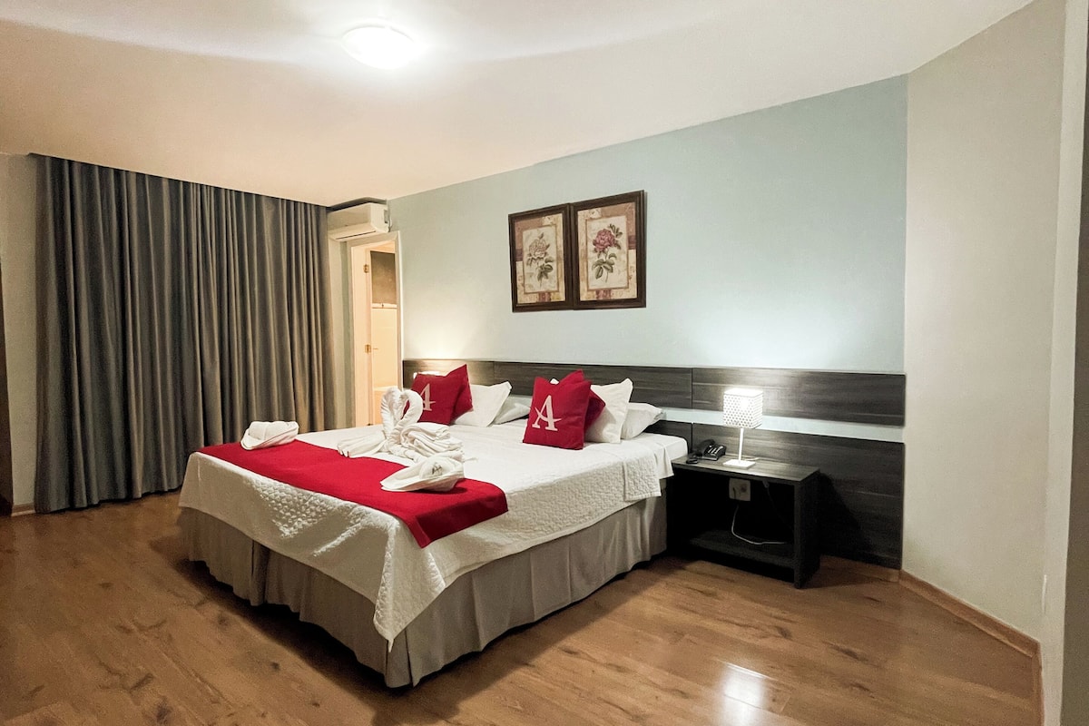 A hotel room with a large bed, a bedside table, a nightstand, and a door leading to another room.