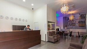 A hotel reception area with a wooden reception desk, multiple clocks, a seating area with sofas, and a mural of a tram on the wall. - Universo Romântico Guesthouse & Spa (Lisbon)