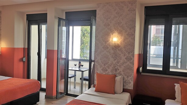 A hotel room with two beds, a balcony with a table and chairs, and a view of the outside. - Universo Romântico Guesthouse & Spa (Lisbon)