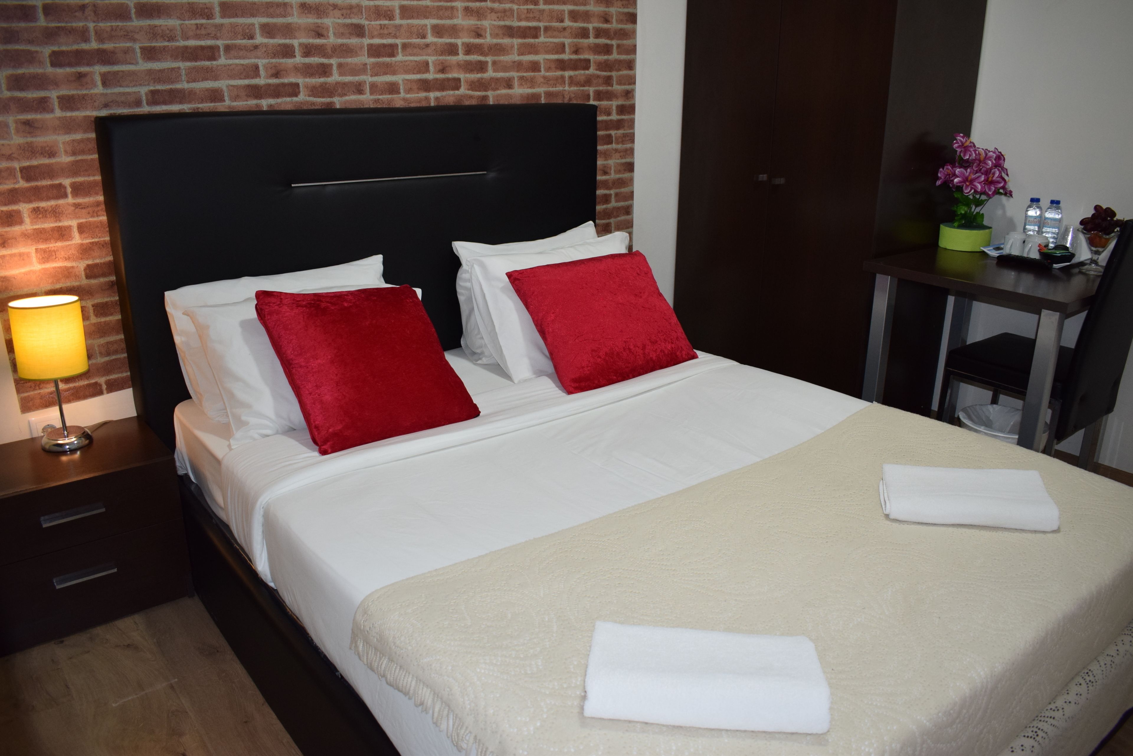 Una cama bien hecha con almohadas blancas y rojas, una manta color beige y dos toallas blancas dobladas.