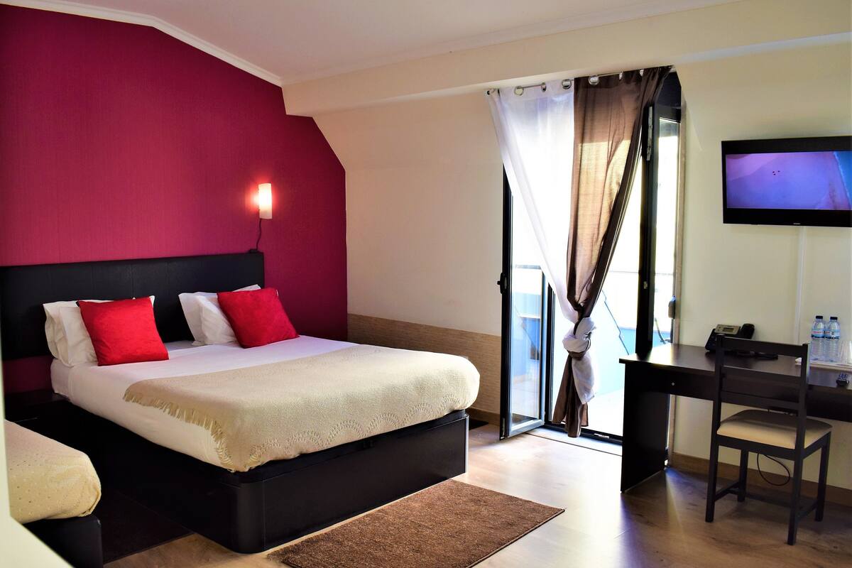 Habitación de hotel con cama, escritorio, silla, televisor y vista por la ventana.