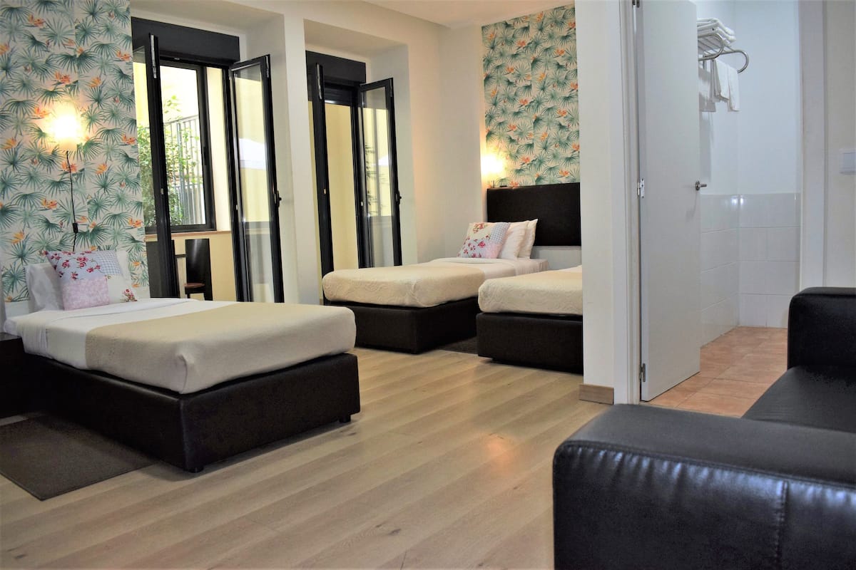 Habitación de hotel con dos camas, un sofá y un baño con toallero.