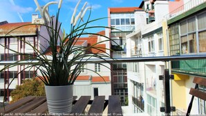 A balcony with a potted plant, wooden bench, and a view of buildings with red roofs and balconies. - Universo Romântico Guesthouse & Spa (Lisbon)