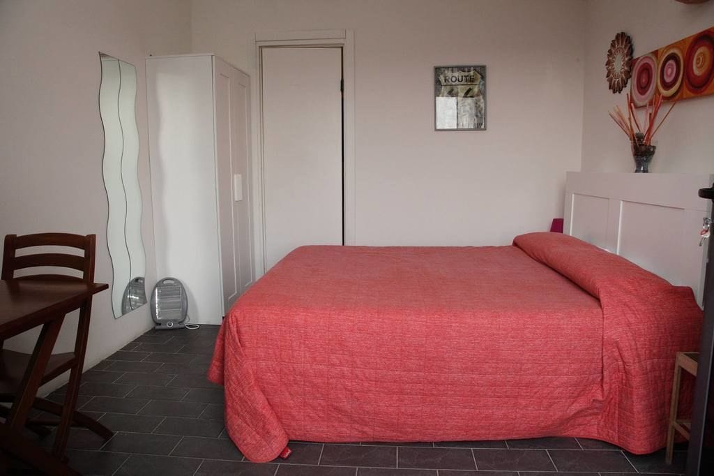 Un dormitorio con cama, una silla, un calentador y una puerta.