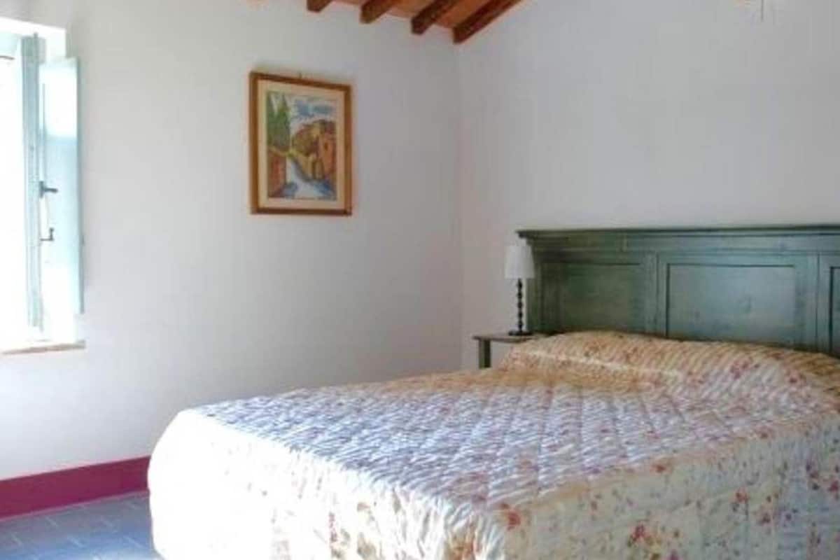 Une chambre  à coucher avec un lit, deux tables de chevet, une commode, une lampe et un tableau encadré au mur.
