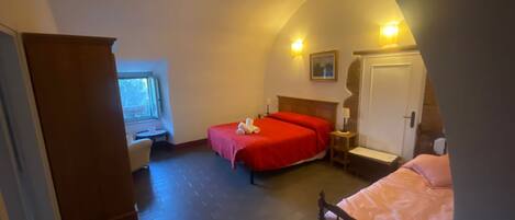 Une chambre d’hôtel avec deux lits, une armoire en bois, une petite table avec une chaise et une fenêtre.
