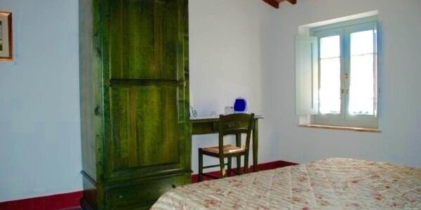 Un dormitorio con cama, un armario de madera, un escritorio con silla y una ventana.