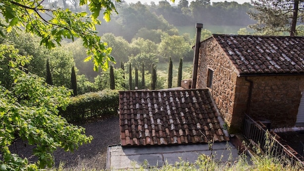 A rustic stone building with a tiled roof, surrounded by lush greenery and tall trees. - Agriturismo Il Sentiero (Acquapendente)