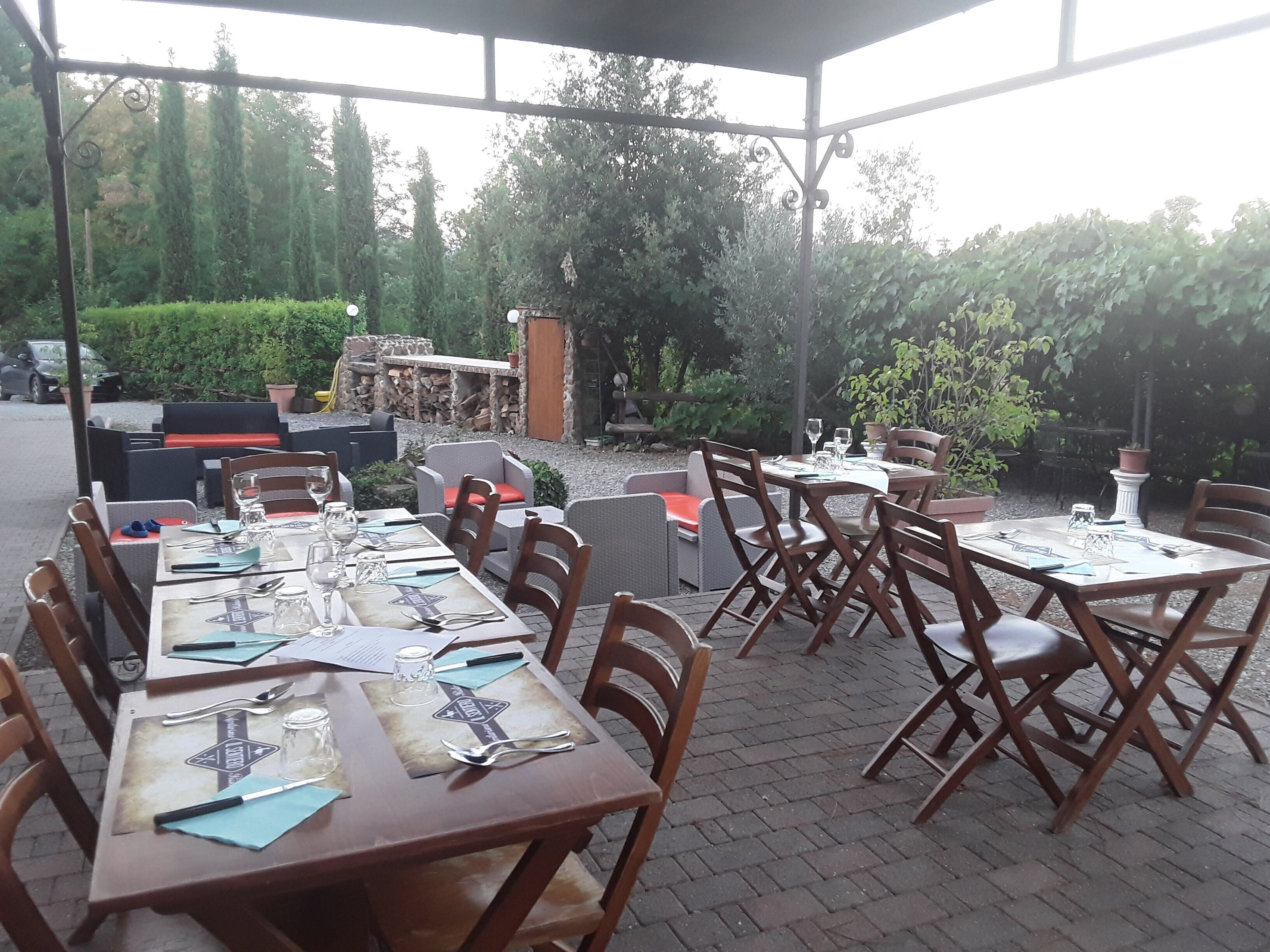 Un área de comedor al aire libre con mesas y sillas, rodeada de follaje y un muro de piedra.