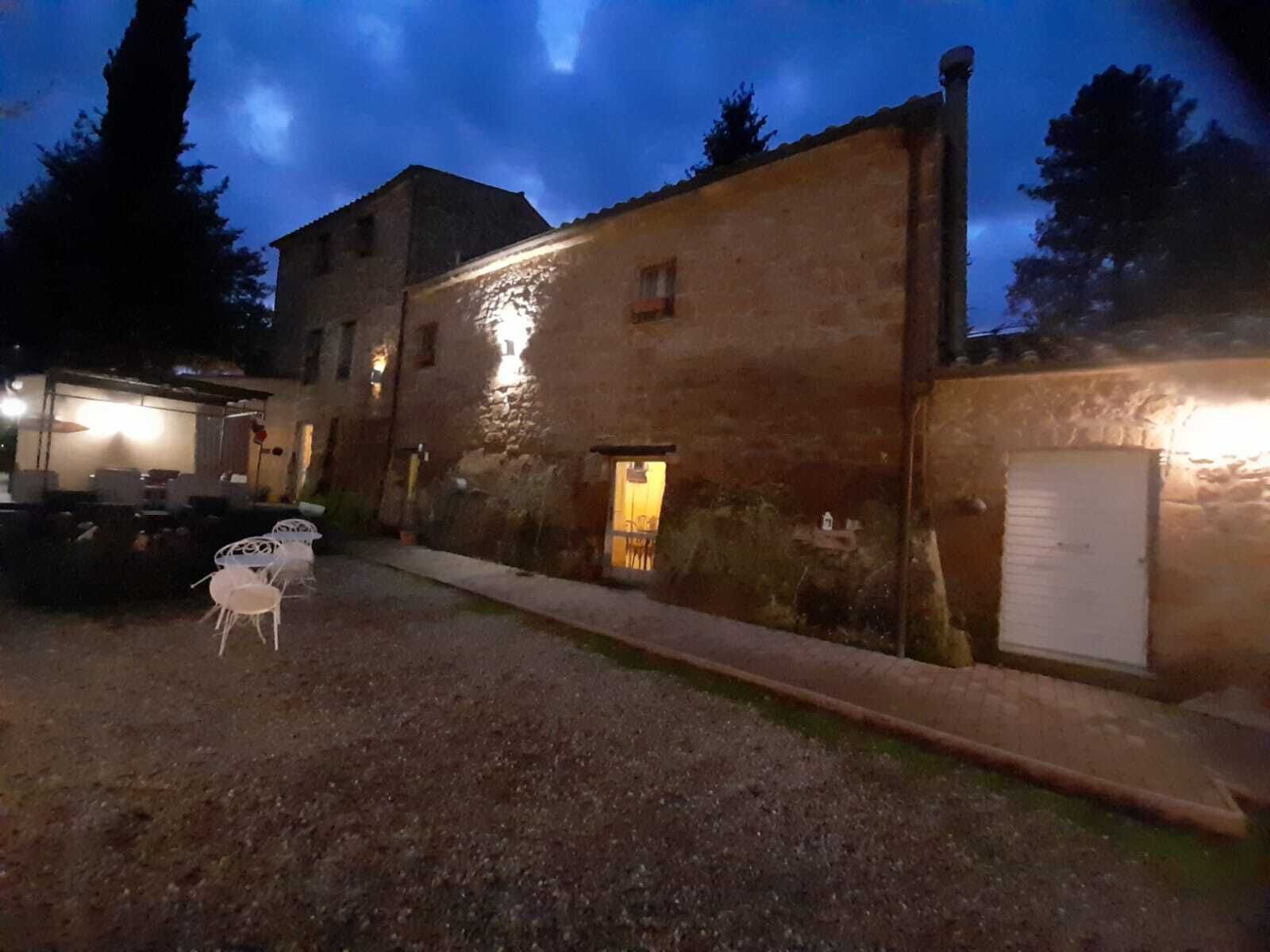 Un edificio rústico con fachada de piedra, una entrada pequeña y un patio empedrado con mesas al aire libre.
