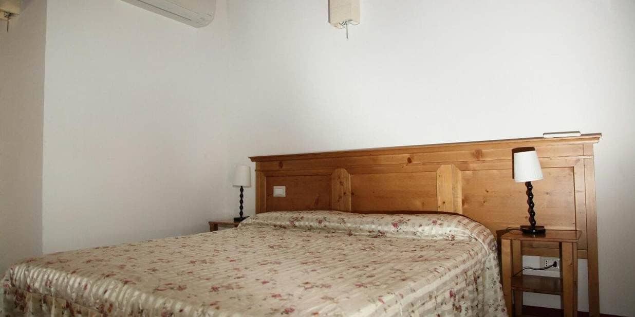 Ein Schlafzimmer mit Holzkopfstütze, einem Bett mit floralem Überwurf, zwei Nachttischlampen und einem Nachttisch mit Lampe.