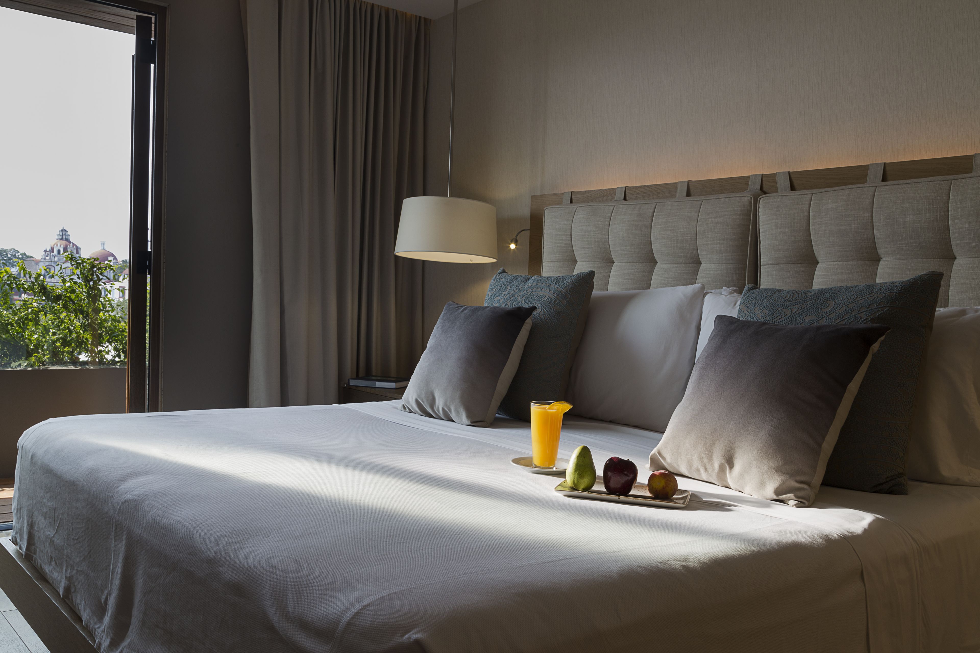 A neatly made bed with pillows, a bedside table with a lamp, and a plate of fruit and juice.