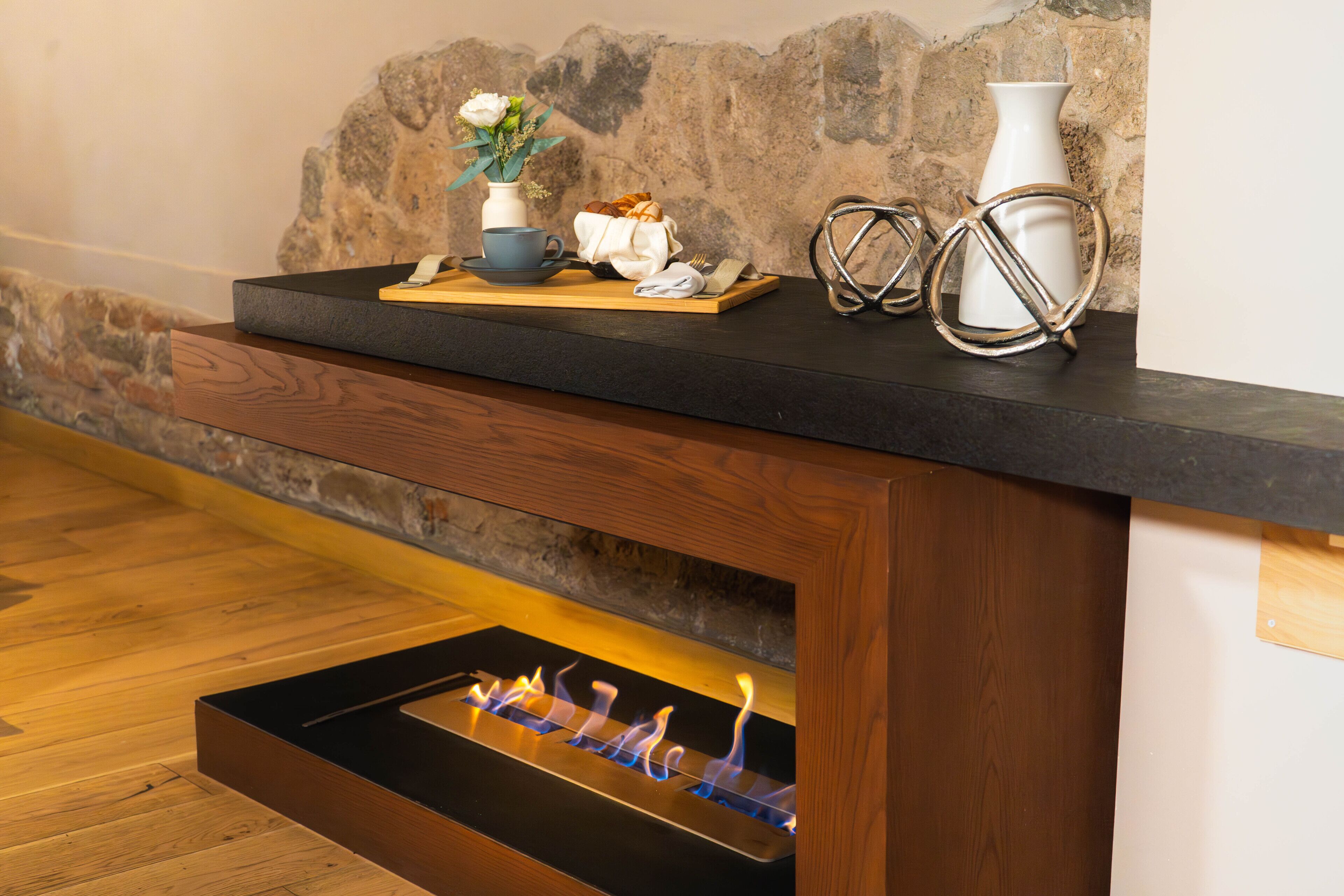 A modern fireplace with a built-in tray table, a stone wall backdrop, and a decorative arrangement on the mantel.
