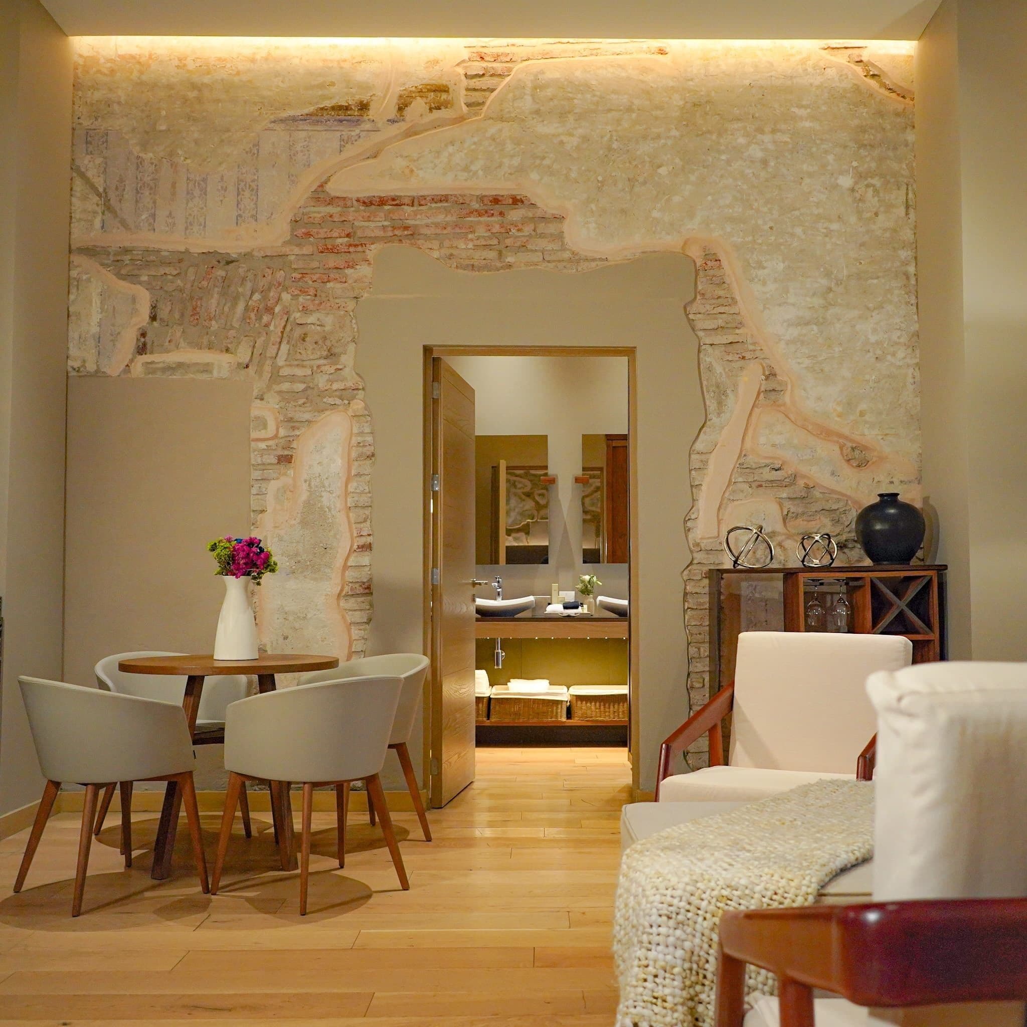 A room with a stone wall, a dining area with chairs and a table, and a sofa.