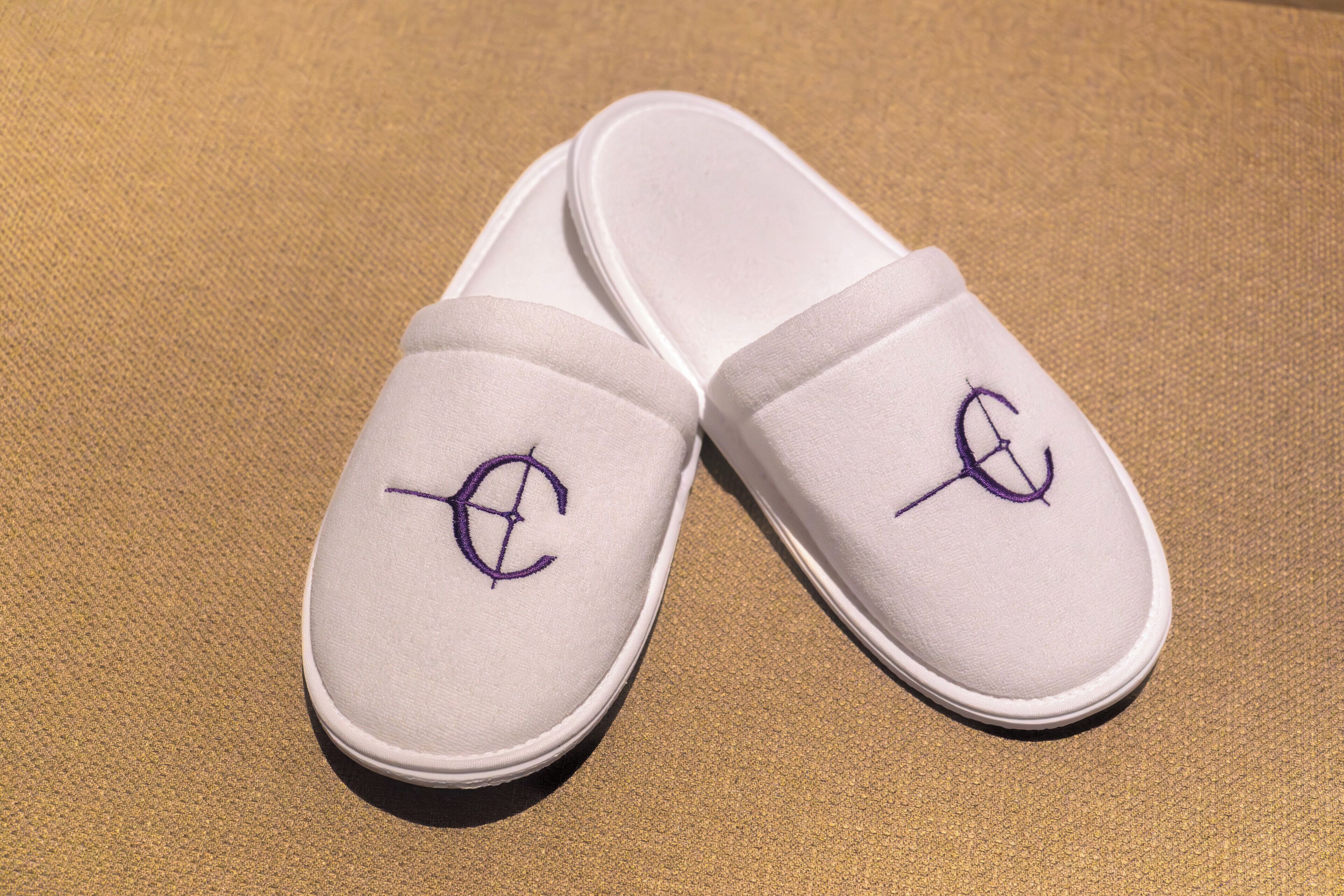Een paar witte slippers met een paars logo op een gestructureerd oppervlak.