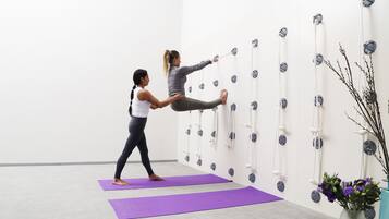 Um estúdio de yoga com tapetes roxos, uma escada de corda fixada na parede e um vaso com flores.