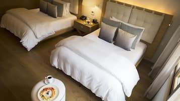 A hotel room with two beds, a bedside table with a lamp, a small round table with a plate of food, and a window with curtains.
