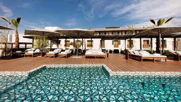 Una piscina al aire libre, sombrillas, sillones reclinables de piscina