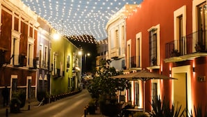 Een smalle straat met gebouwen aan beide zijden, lampionnen erboven en terrasjes met parasols.