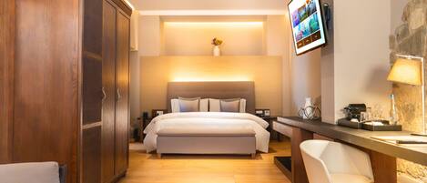 A modern hotel room with a large bed, a wooden wardrobe, a desk with a chair, and a mounted TV.