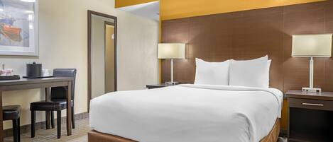 A hotel room with a large bed, two bedside tables with lamps, a desk with a chair, and a framed picture on the wall.
