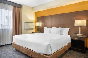 A hotel room with a large bed, two bedside tables with lamps, a headboard, and a window with curtains.