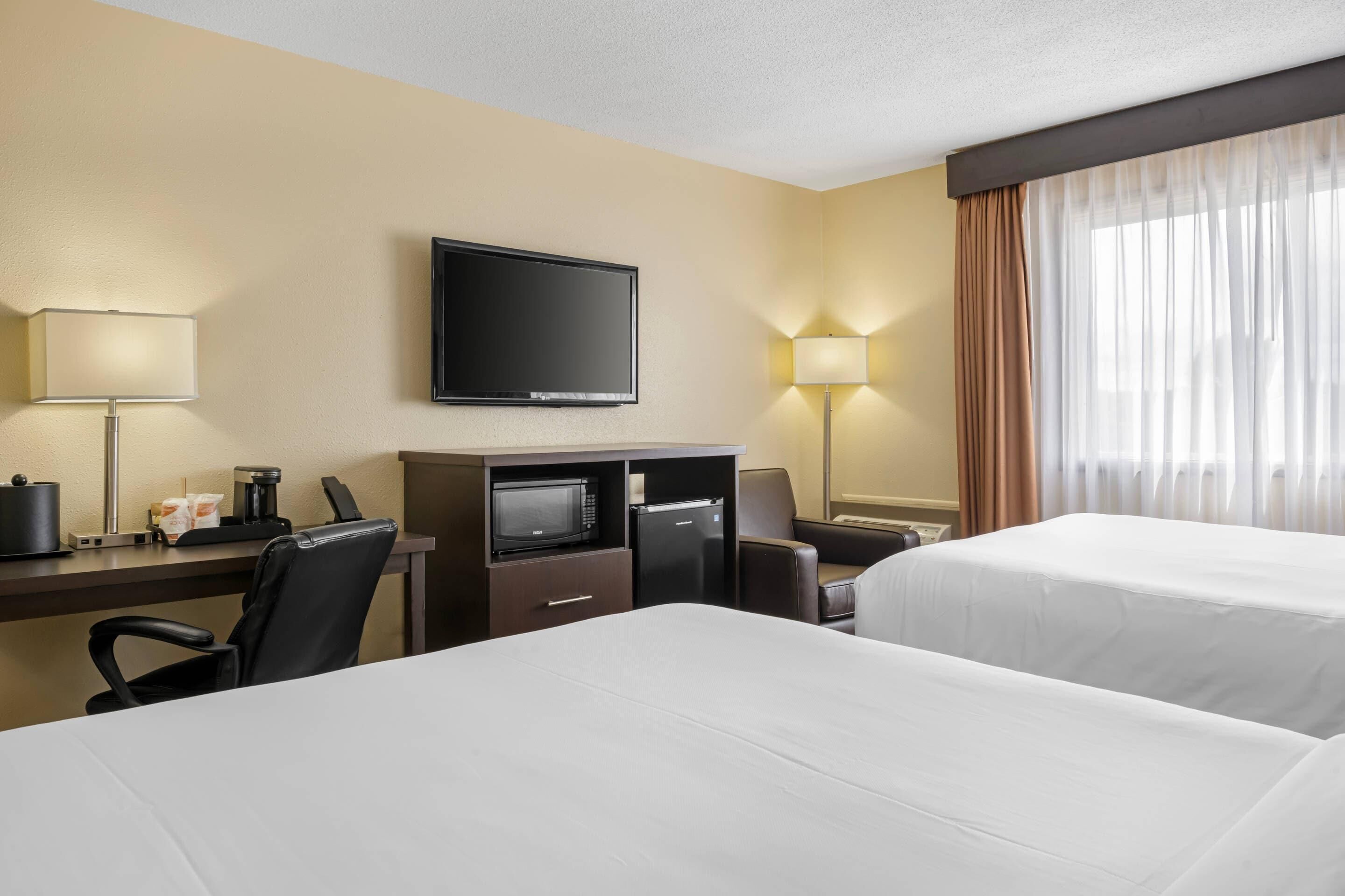 A hotel room with two beds, a desk with a television, a coffee maker, and a microwave.