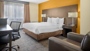 A hotel room with a large bed, two bedside tables with lamps, a desk, and a chair. - Quality Inn & Suites Bathurst (Bathurst)