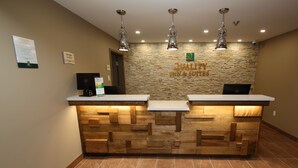 A reception desk with a stone wall backdrop, two computer monitors, and a sign reading "Quality Inn & Suites". - Quality Inn & Suites Bathurst (Bathurst)