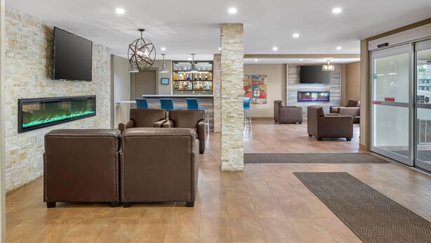 A modern lobby with a stone wall, a large flat-screen TV, a fish tank, leather sofas, and a bar area with shelves of bottles. - Quality Inn & Suites Bathurst (Bathurst)