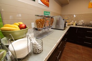 A buffet setup with bowls of fruits, cereal, and a sign labeled "healthy".