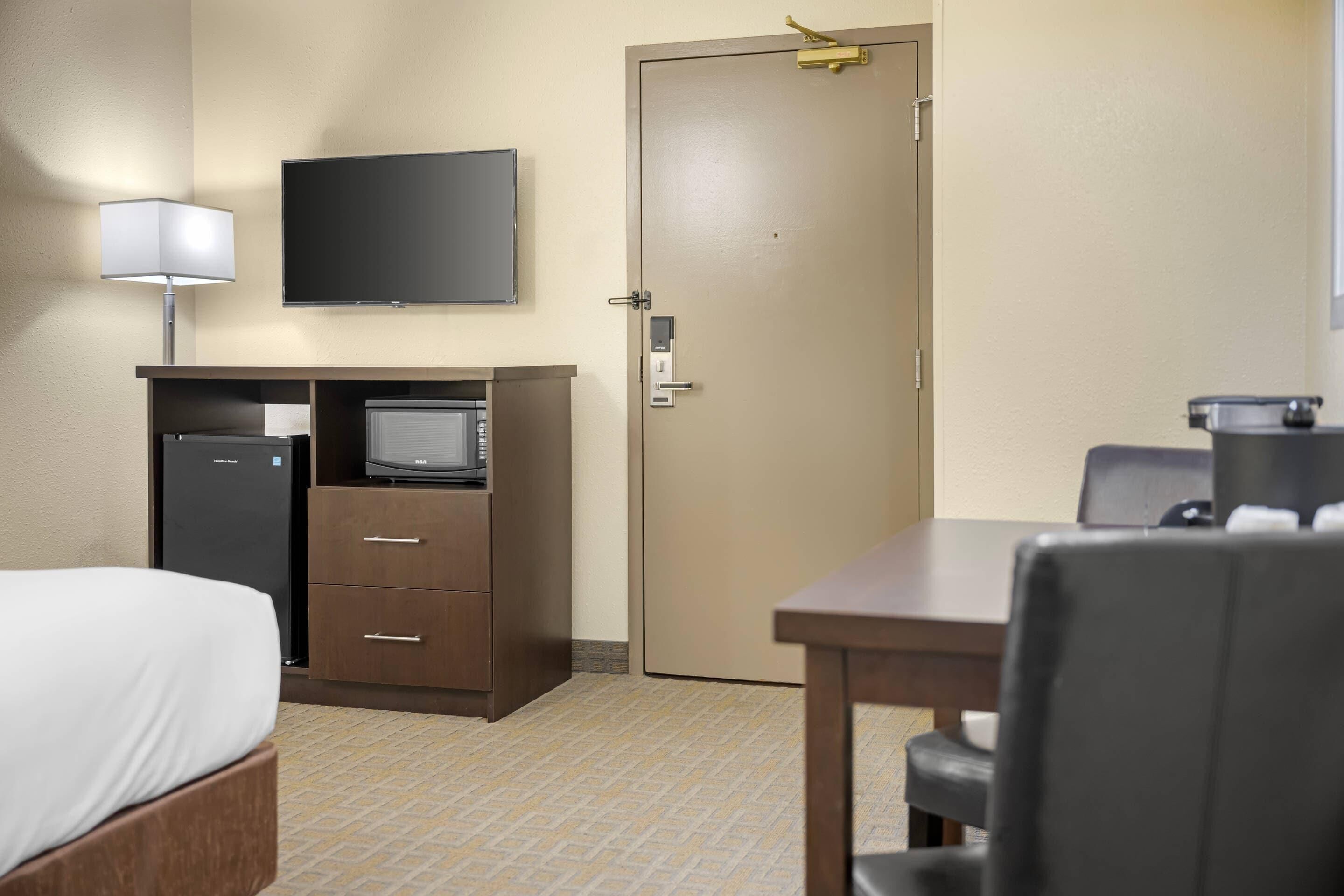 A hotel room with a bed, a desk with a computer, a television, a door, and a table with chairs.