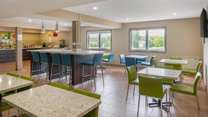 A modern dining area with a kitchen in the background, featuring bar stools, tables, and chairs. - Quality Inn & Suites Bathurst (Bathurst)