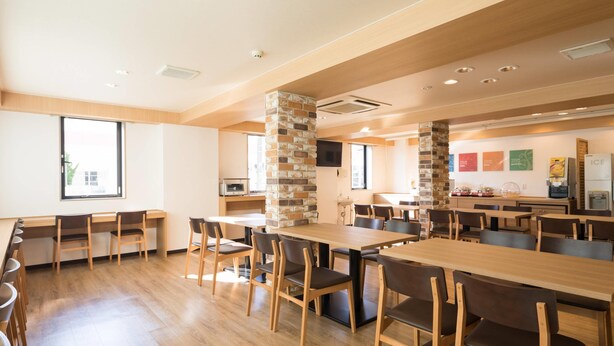 Un comedor amplio con varias mesas y sillas de madera, un pilar de piedra y una zona de cocina al fondo.