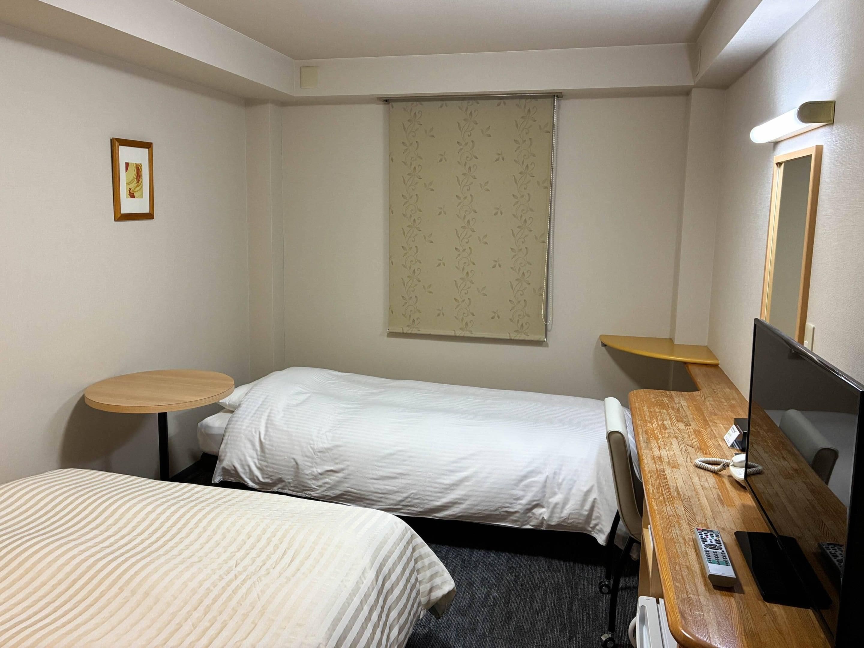 A hotel room with two single beds, a desk with a computer, a telephone, and a small table.