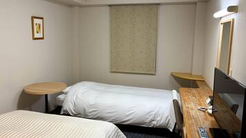 A hotel room with two single beds, a desk with a computer, a telephone, and a small table.